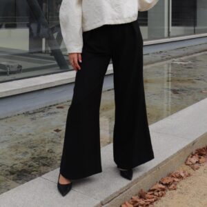 Détail d’un pantalon noir Alibee Couture porté avec un haut blanc texturé, soulignant la coupe fluide et la qualité du tissu.