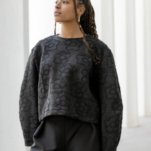 Femme portant un pull noir texturé à fleurs ton sur ton signé Alibee Couture, associant élégance et originalité.